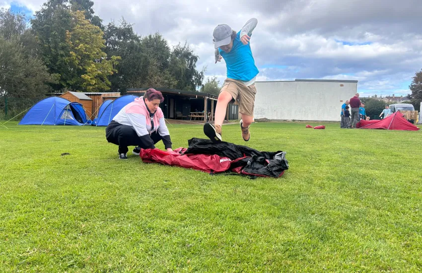 a beaver jumping over a rolled tent while a leader unrolls it