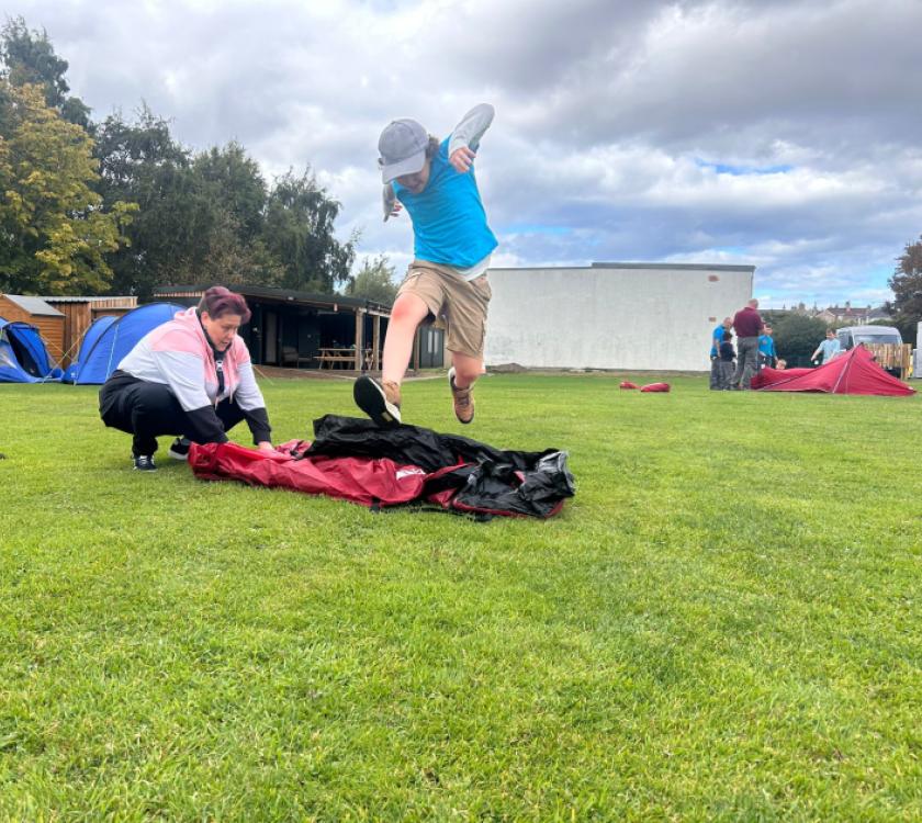 a beaver jumping over a rolled tent while a leader unrolls it